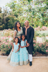 beautiful indian family with daughters girls sisters hugging in close with a bindi and traditional sari dress and kurta in a garden with flowers