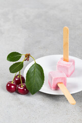 Two Cherry ice creams in the shape of small cubes on a wooden stick. On a plate. Copy space