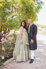 beautiful indian couple hugging in close with a bindi and traditional sari dress and kurta in a garden with flowers