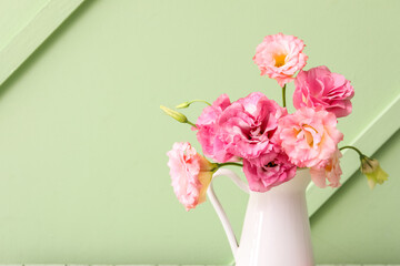 Jug with beautiful pink eustoma flowers on green background