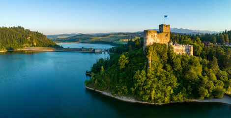 Poland. Medieval castle in Niedzica, 14th century (upper part) in sunset light. Artificial Czorsztyn lake on Dunajec river, damn and hydro power station. Tatra Mountains in the background. Aerial view