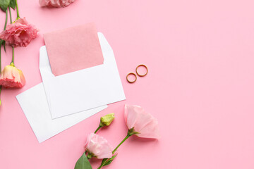 Composition with blank cards, envelope, wedding rings and beautiful eustoma flowers on pink background