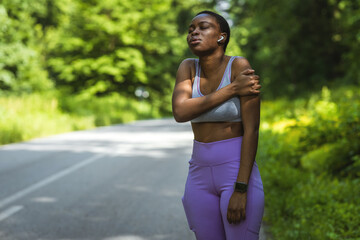 Active young black woman holding her shoulder in pain while exercising outdoors. Athlete suffering...