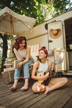Happy hippie girls are having a good time with playing on guitar in camper trailer. Holiday, vacation, trip concept.