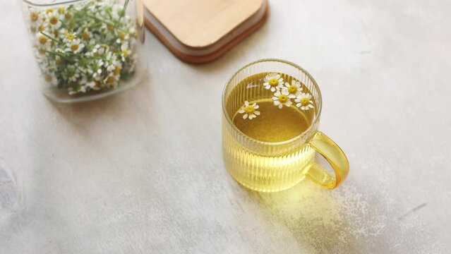 A cup of Chamomile tea on light wooden table with flowers in glass container 