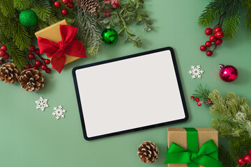 Christmas concept with digital tablet mock up, gift boxes and festive decorations on green background. Top view, flat lay