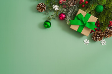 Christmas concept with gift box, pine tree branches and festive decorations on green background. Top view, flat lay