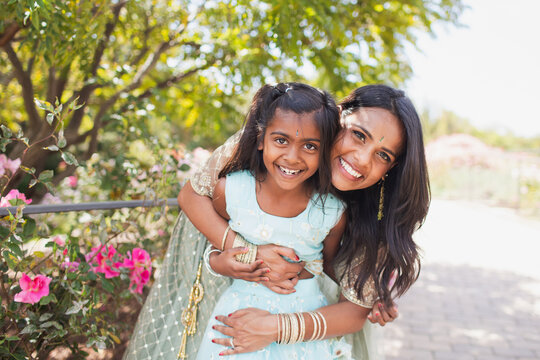 beautiful indian mother and daughter hugging in close with a bindi and traditional sari dress and in a garden with flowers