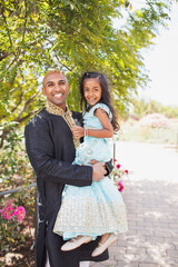 beautiful indian father and daughter hugging in close with a bindi and traditional sari dress and kurta and in a garden with flowers
