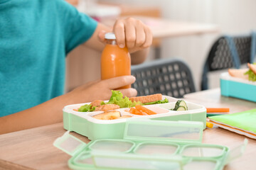 Obraz na płótnie Canvas Little boy with bottle of juice having lunch in classroom, closeup