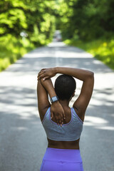 One african american female athlete with an afro listening to music on her earphones while exercising outdoors in nature. Dedicated black woman smiling while warming up before a workout outside