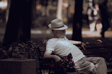 Fototapeta na wymiar Stylish man in white. White. Gray beard. White hat. Peaceful old age. Old parents. Noble gray hair. A man on a bench.