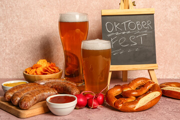 Glasses of cold beer, chalkboard with word OKTOBERFEST and different snacks on pink background