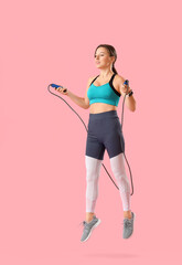 Fototapeta na wymiar Sporty young woman jumping rope on pink background