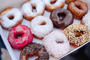 Yummy colorful doughnuts in glaze and sprinkles, lying in a paper box. Chocolate doughnuts, powdered sugar, ground peanuts, coconut shavings