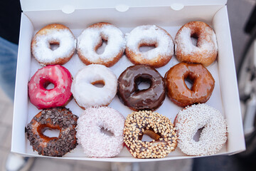 Yummy colorful doughnuts in glaze and sprinkles, lying in a paper box. Chocolate doughnuts, powdered sugar, ground peanuts, coconut shavings