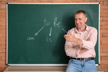 Male teacher conducting English grammar lesson near blackboard in classroom