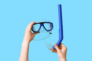 Male hands with snorkeling mask and tube on blue background
