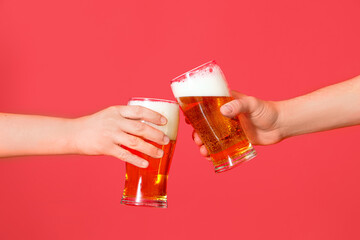 Man and woman with glasses of cold beer clinking on red background