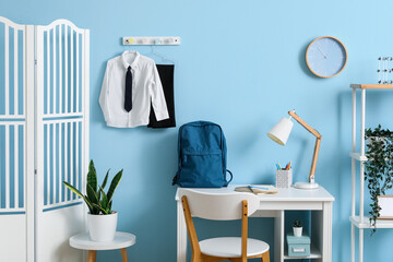 Interior of workplace with desk, shelving unit, folding screen, clock, backpack and stylish school...