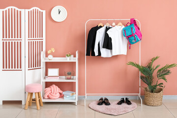 Rack with stylish school uniform, backpack, shoes, shelving unit and folding screen near beige wall in room