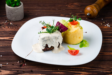 Beef steak with mashed potatoes, tomatoes, lettuce, herbs and sauce in a plate.