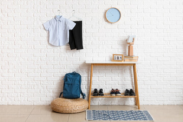 Fototapeta na wymiar Table with shoes, backpack, clock and stylish school uniform hanging on light brick wall in room