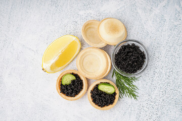 Tasty tartlets with black caviar on grey background