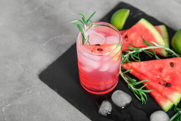 Board with glass of tasty watermelon cocktail, lime and ice cubes on grunge grey background