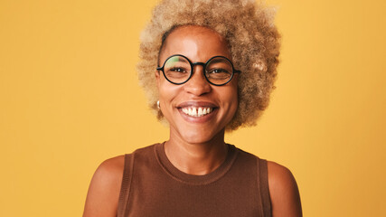 Close-up of girl in glasses, wearing brown top laughing woman looking at camera isolated on orange background