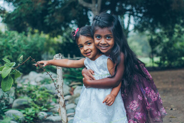 beautiful indian sisters girls hugging in the park with trees and greenery