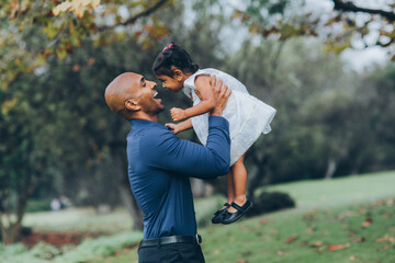 beautiful indian father playfully hugging his child daughter girl in the park with trees and greenery