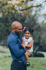 beautiful indian father playfully hugging his child daughter girl in the park with trees and greenery