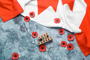 Poppy flowers with flag of Canada and text LEST WE FORGET on grunge blue background. Remembrance Day