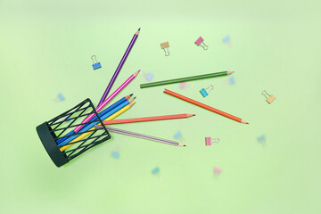 Overturned pen cup with colorful pencils and paperclips on green background