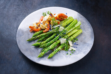 Green asparagus glazed with fried king prawns and parmesan cheese served as close-up on a design plate with text space