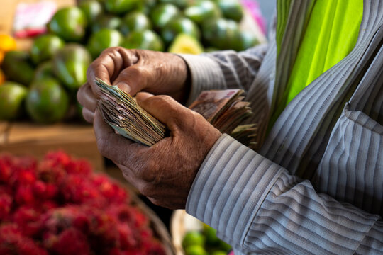 Old Man Hands Count Lempiras (Money Bills) by a Bunch of Ripe Rambutan and Avocados by a Stall in Colorful Market "Mercado Mayoreo"