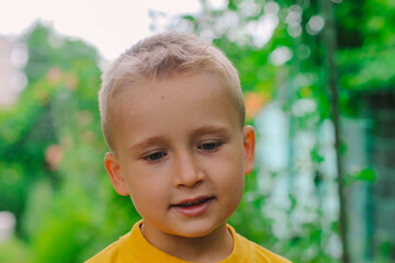 portrait of a beautiful child boy close-up in a yellow t-shirt against the background of a green garden selective focus