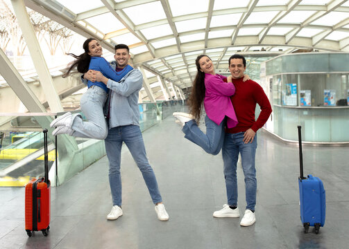 Two Women Jumping And Hugging Their Husbands Posing At Airport