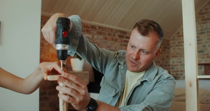 A man and a woman assemble a shelving at home, they use a screwdriver, talk and smile sitting on the floor
