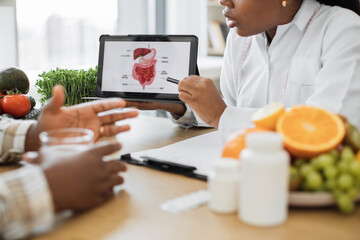 Close up view of digital device with photo of digestive system being used by multicultural lady in doctor's coat. Nutrition specialist clarifying diet-caused complications during GI treatment.