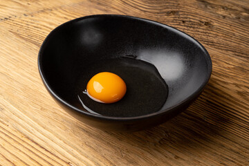 One Broken Egg in Black Bowl, Raw Yolk and White, Fresh Broken Organic Chicken Egg