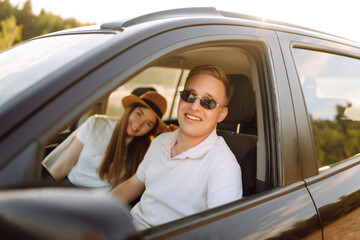 Young couple in a new car is relaxing in the sunset. Man has fun with a girl in a car at the wheel. Travel, tourism, recreation.