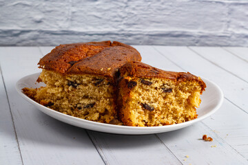 An English cake cut in half on a white dish on a white wooden table. Selective focus