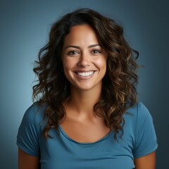 Fototapeta premium Portrait of a smiling middle aged Latin woman with brown hair on blue background. Happy middle aged Latin American woman with a smile and wavy hair in blue shirt. Cheerful woman with shiny white teeth