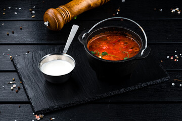 Solyanka soup with ham, meat, olives, tomatoes, sour cream and microgreens in a bowl.