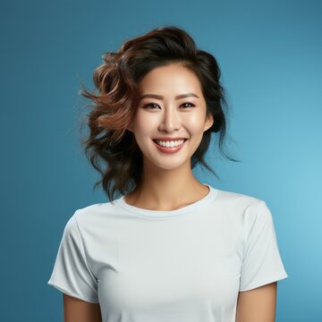 Portrait of a smiling middle aged Asian woman with black hair on a blue background. Happy middle aged Asian woman with smile and wavy hair in white shirt. Cheerful Chinese woman with shiny white teeth