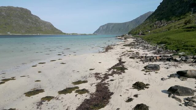 survol d'une plage de sable blanc et d'un bras de mer aux eaux translucides entour&eacute;e de montagnes vertes