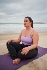 Fototapeta na wymiar Full figured woman meditating at gloomy beach in the morning