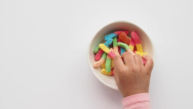 top view of child hand pick colorful candy sweet jelly in a bowl on table 